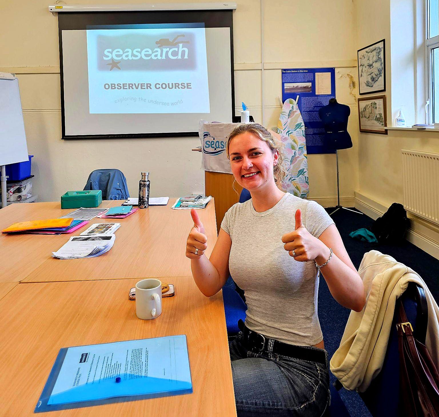 Person giving thumbs up in classroom with Seasearch Observer Course displayed on screen.