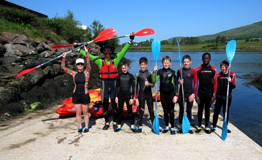 Group of eight people in wetsuits holding paddles by a river.
